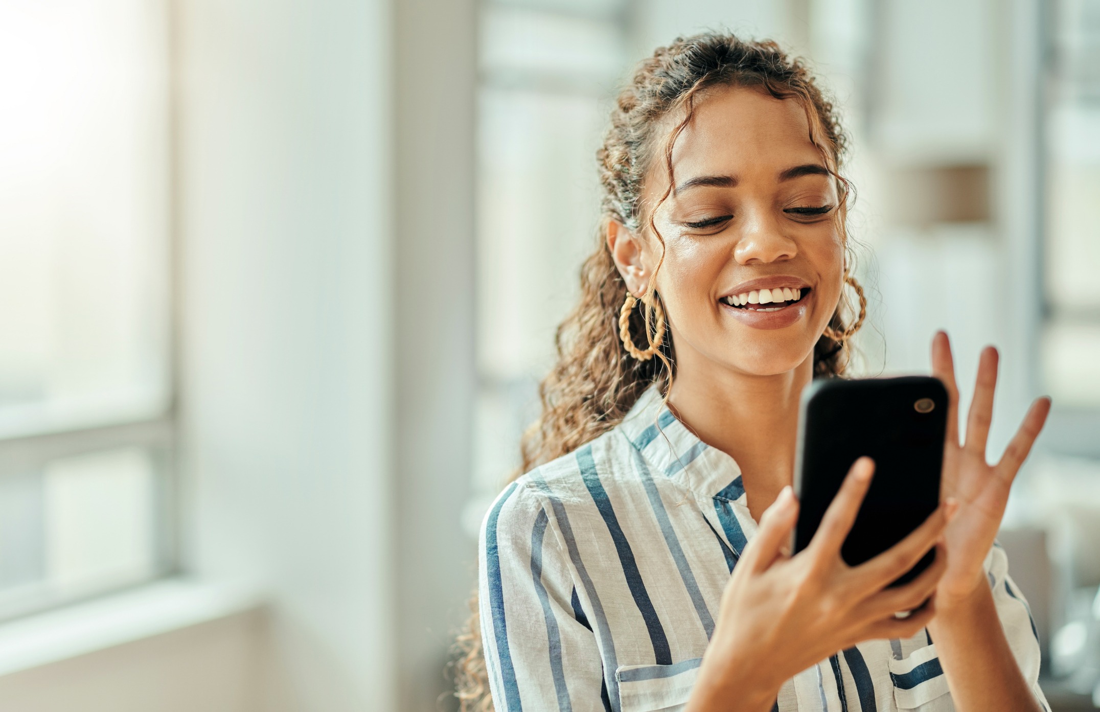 A woman smiles as she uses her phone to access an app