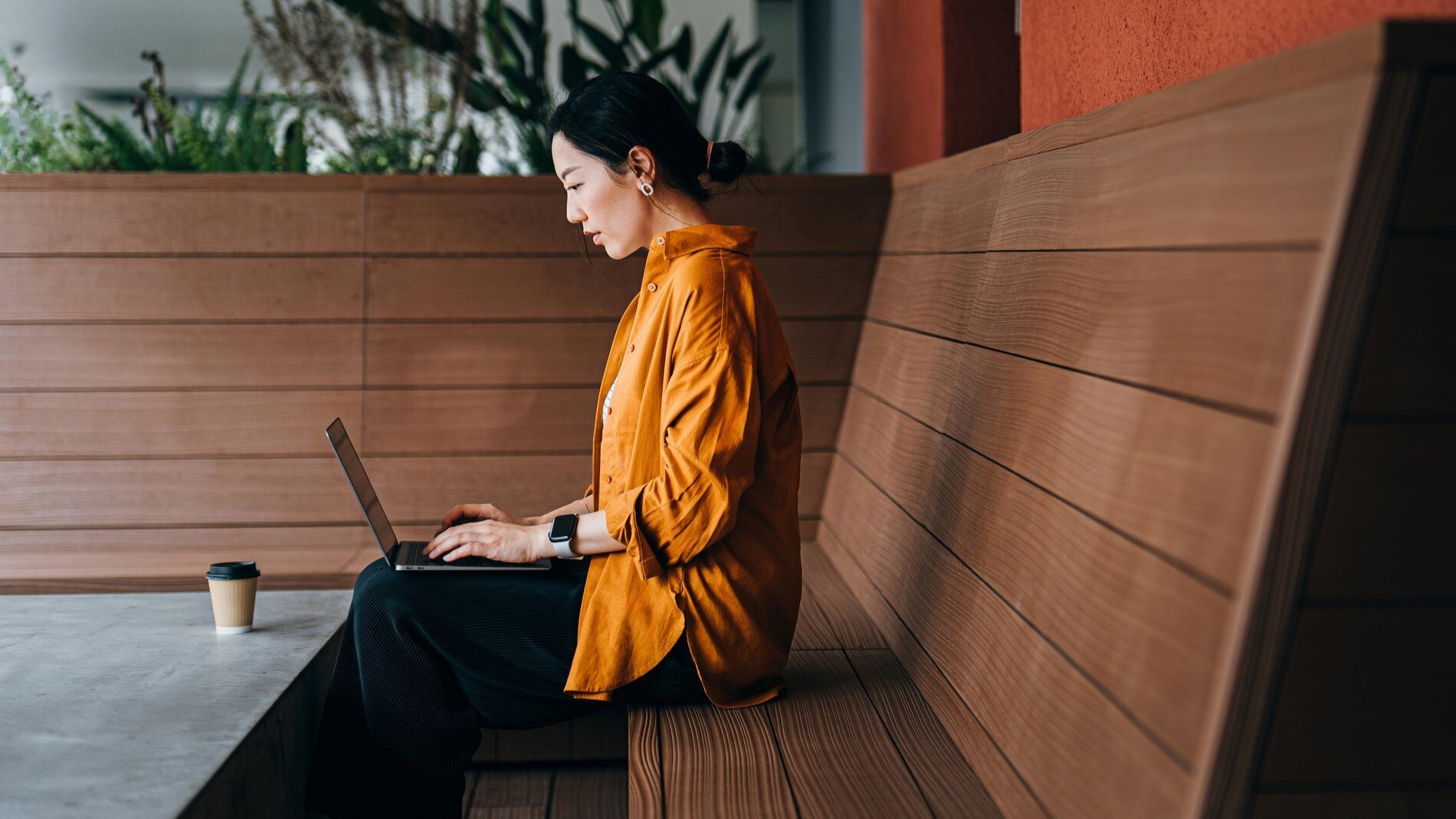woman sitting on bench while typing on laptop