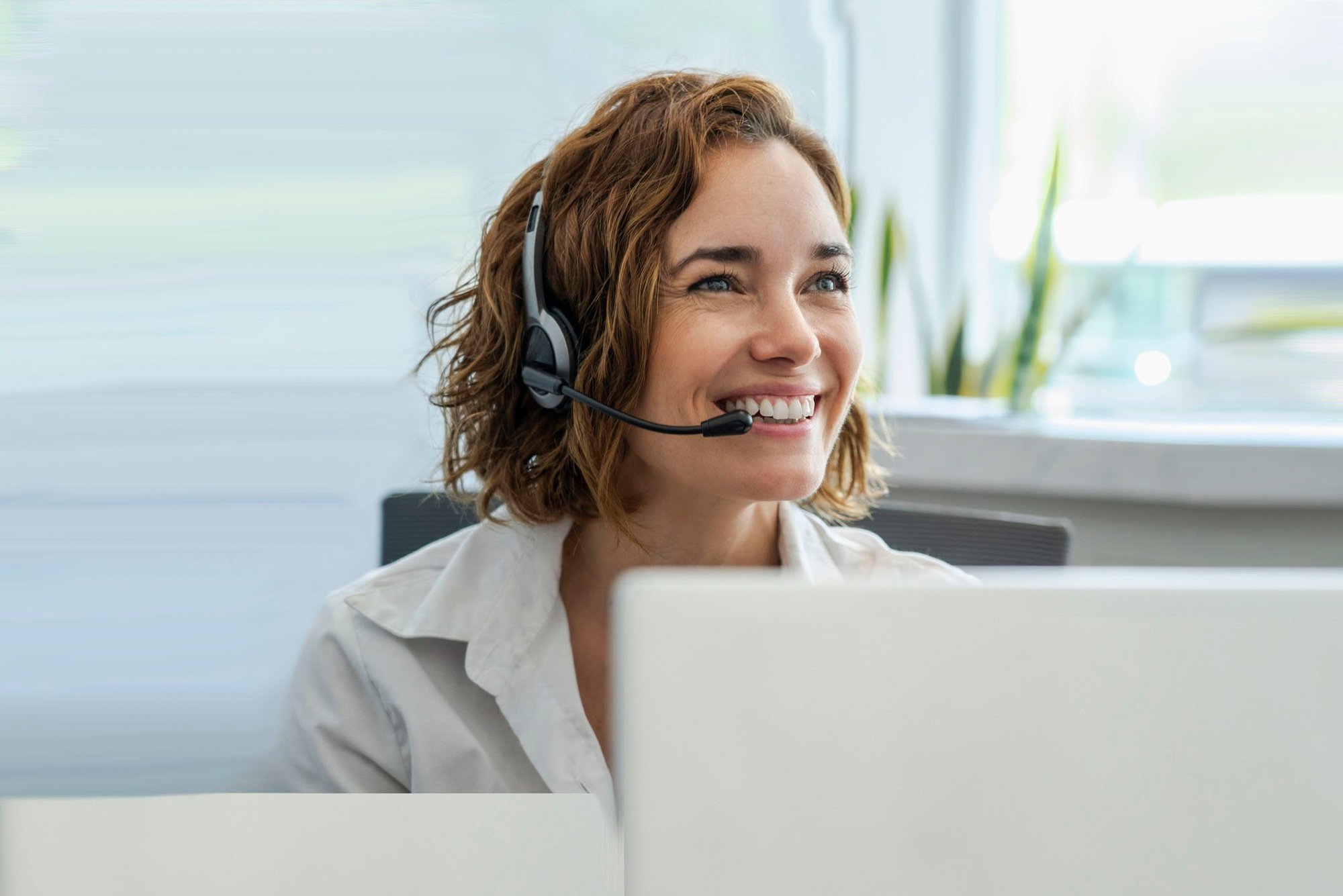 A front desk worker smiles as she speaks to a patient with an interpreter on the line