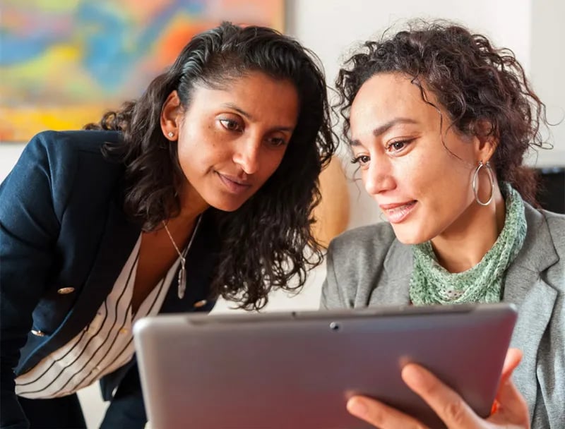 Two women look at the AI Translation App on a tablet.