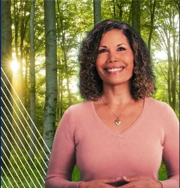 Angela Witmer smiles in front of a stand of trees.
