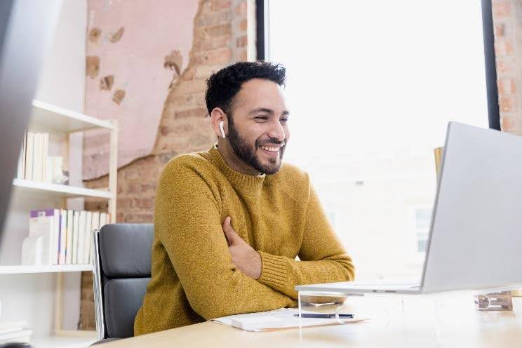 A man smiles as he works on his computer in an office.