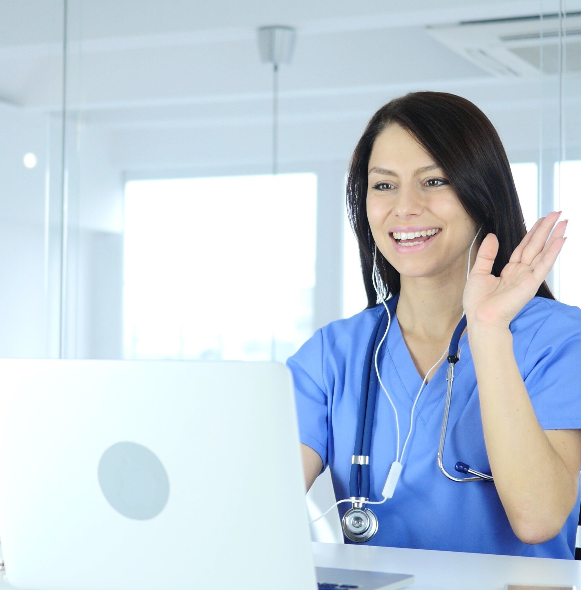 A caregiver wearing headphones waves to the screen during a video interpreting session