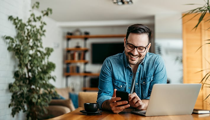man using cell phone while sitting in front of a laptop