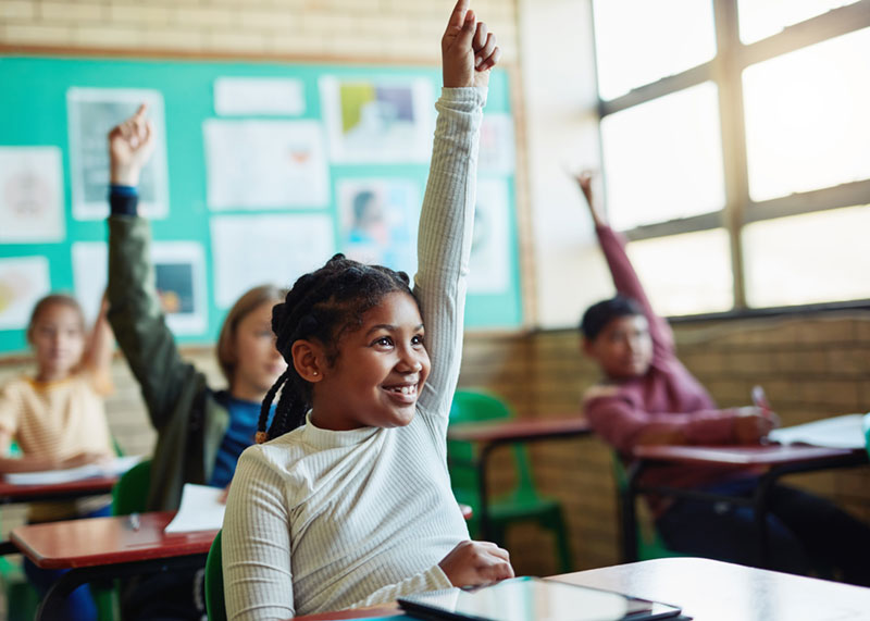 A girl with her hand up in a school classroom
