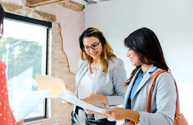 A group of women stand in an office and discuss some documentation with a smile.