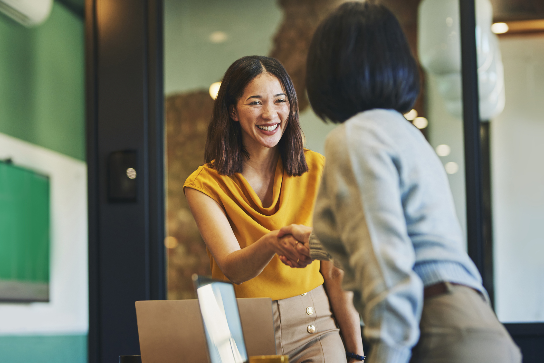 Two business women smile and shake hands in an office
