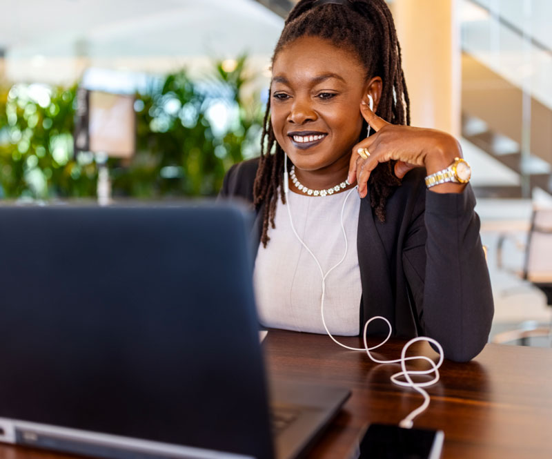 A smiling woman wearing earbuds smiles as she listens to and watches translated videos on a laptop.