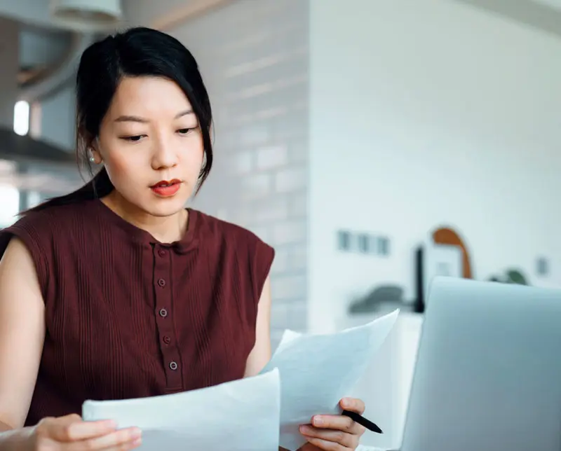A linguist looks a paper documentation as she works on a translation on her computer